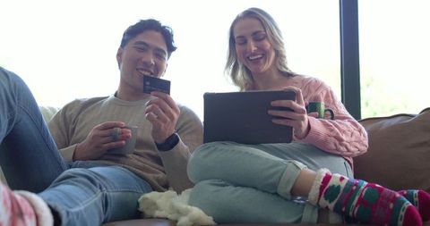 Couple relaxing and shopping online on tablet while holding credit card and mugs