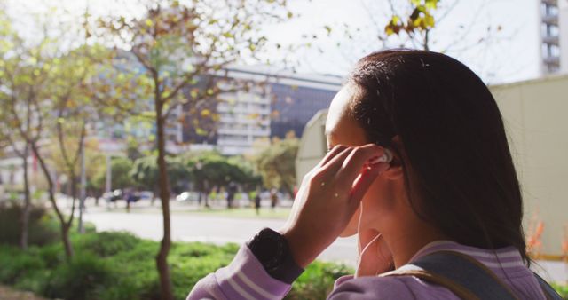 Woman Adjusting Earbuds while Walking in Urban Park - Download Free Stock Images Pikwizard.com