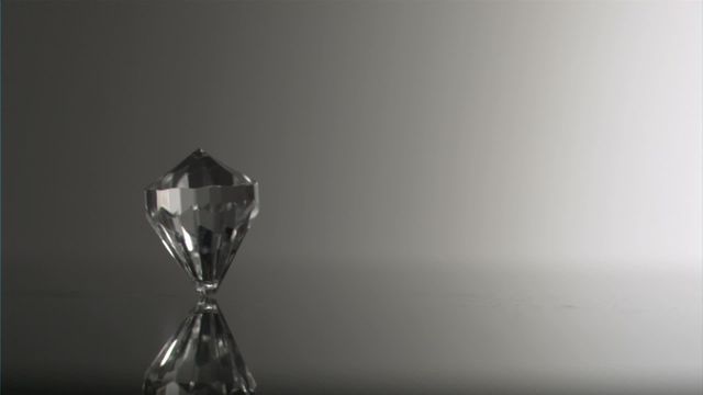 A single clear diamond prominently stands against a subtle gradient background, its facets glimmering while casting a soft reflection. The minimalist and dramatic effect captured reflects the concept of luxury and timeless beauty, making it suitable for use in jewelry marketing materials, luxury brand advertising, or high-end design catalogs aiming to convey opulence and refinement.