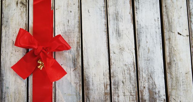 A vibrant red ribbon with a bow is tied around a rustic wooden background, with copy space. Its presence suggests a gift or celebration theme, perfect for festive and holiday-related designs.