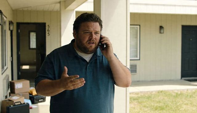 Man making phone call on motel porch reacting to packages and luggage