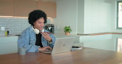 Mid adult african american man working at kitchen island typing on laptop and using smartphone