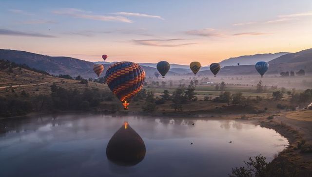 Dawn hot air balloons floating over misty valley lake with glowing burner calm reflection