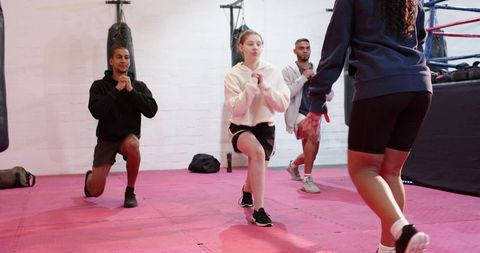 Diverse group performing synchronized lunges in boxing gym building strength and teamwork