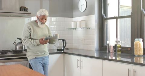 Senior Man Relaxing in Modern Kitchen with Mug and Smartphone