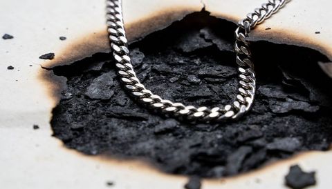 Polished silver curb chain resting on charred paper and ash macro jewelry detail