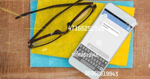 Smartphone showing text message with numeric overlay, keyboard, glasses and colorful notebooks