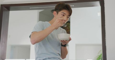 Asian Teenager Eating Breakfast Alone at Home in Modern Living Room