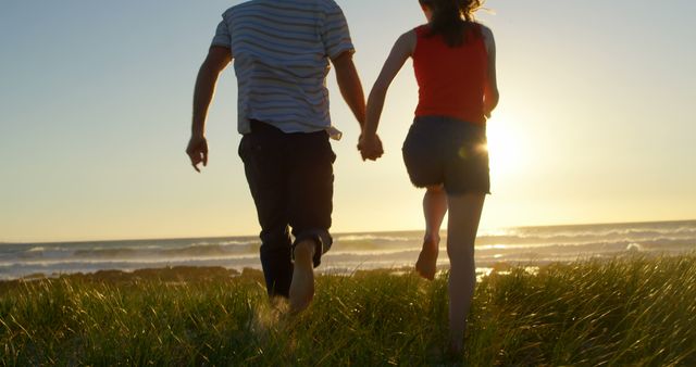 Couple running towards ocean holding hands during sunset, symbolizing love, joy, and romance. Perfect for marketing campaigns, travel brochures, romantic films, couples therapy promotions, and lifestyle blog visuals.