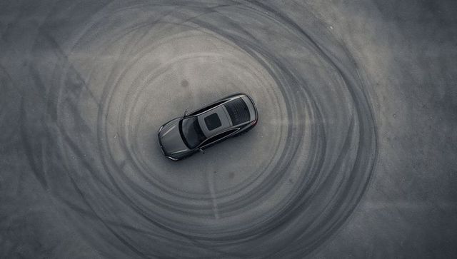 Aerial view dark gray sedan creating concentric skid marks on empty asphalt lot