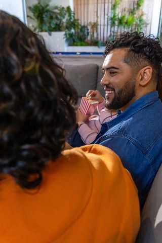 Young couple relaxing on couch watching movie and sharing popcorn in cozy modern lounge