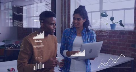 Coworkers collaborating and analyzing business data with laptop and charts in loft office