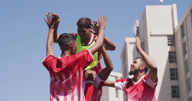 Soccer teammates celebrating a victory in an urban outdoor setting, lifting a player in the center while high-fiving. Ideal for illustrating team spirit, celebration of success, sports enthusiasm, teamwork, athletic achievements, and camaraderie. Perfect for sports magazines, athletic brand advertisements, and motivational posters.