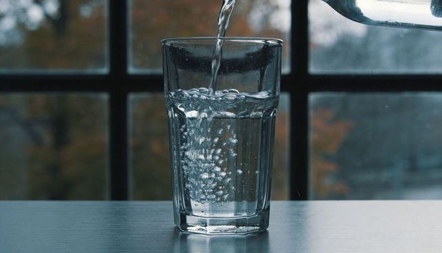 Pouring Water into Faceted Glass by Paned Window with Autumn Bokeh, Bubbles