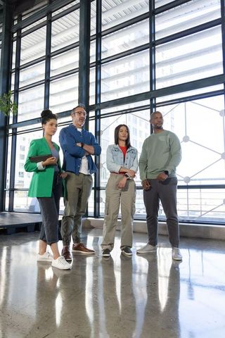 Diverse corporate team standing in modern glass atrium projecting confidence, collaboration