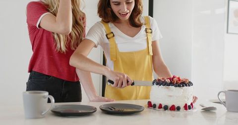 Young women cutting berry cake at modern kitchen island, bright home baking celebration