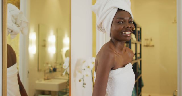Portrait of smiling african american woman next to mirror with towel in bathroom. health and beauty concept.