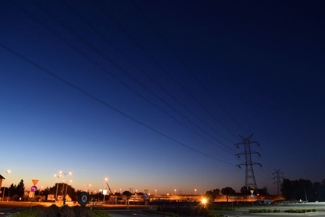 This image captures the early morning urban landscape with visible power lines and illuminated city lights against a soft blue sky. Ideal for illustrating themes about urban infrastructure, electricity, and early hours in the city. Great for use in websites, presentations, and articles related to urban planning, energy, and city life.