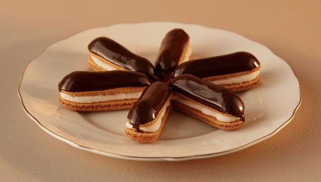 Chocolate eclairs forming star on gold-rim porcelain plate with glossy chocolate glaze