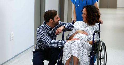 Pregnant Woman Supported by Partner in Hospital Corridor