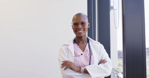 Confident african american doctor smiling with arms crossed in bright modern urban clinic
