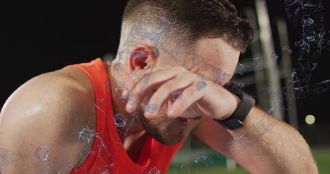 Runner wiping sweat on night track wearing fitness watch with neon digital mesh