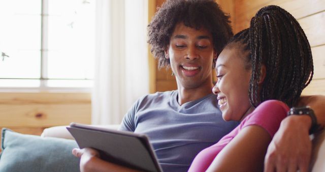 Happy african american couple spending time in log cabin using tablet. Log cabin and lifestyle concept.
