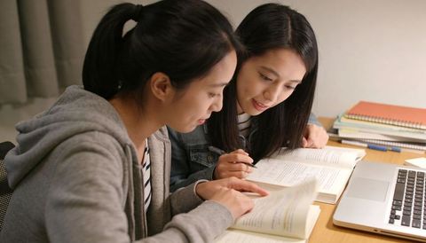 Two Students Collaborating Over Textbooks and Laptop, Late Night Exam Study Session
