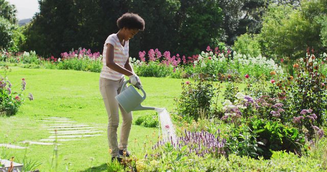 Happy african american teenage girl watering plants in sunny garden - Download Free Stock Photos Pikwizard.com