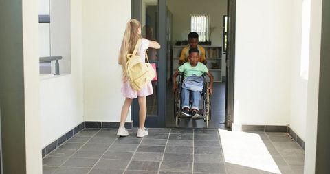 Diverse students helping wheelchair user through school doorway, inclusion and teamwork