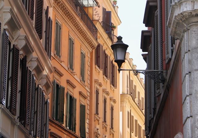 This photo showcases a narrow street lined with historical buildings in warm colors, each adorned with wooden shutters and iron balconies. A classic street lamp is prominently featured, adding to the old-world charm. Perfect for illustrating travel destinations, European architecture, romantic getaways, or urban exploration themes.