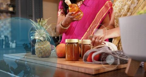 Indian women in saris preparing homemade preserves, arranging jars and fruit on counter
