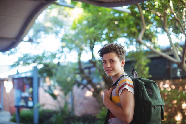 This image shows a cheerful schoolboy standing outdoors on a school campus, carrying a backpack. Ideal for educational materials, school brochures, back-to-school promotions, and youth-related content.