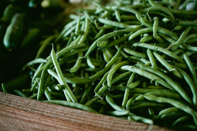 Fresh green beans lying in a wooden crate. Perfect for showcasing fresh produce, organic farming, or health and nutrition articles. Suitable for use in grocery store promotions, recipe blogs, and agricultural discussions.