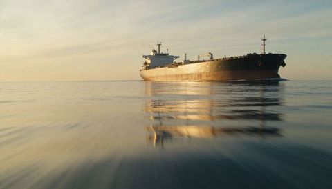 Oil tanker sailing at golden hour with calm sea reflection, horizon and marine navigation