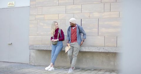 Diverse young friends leaning and chatting against urban tiled wall