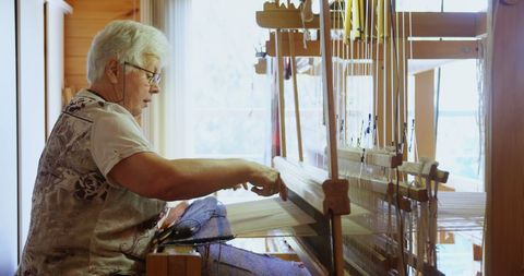 Senior Woman Weaving Cloth on Handloom in Cozy Workshop