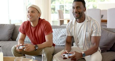 Friends playing video games on sofa in bright living room during casual multiplayer session