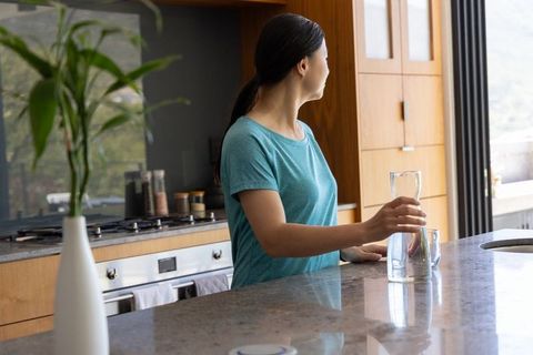 Asian woman holding glass carafe at modern minimalist kitchen island natural light