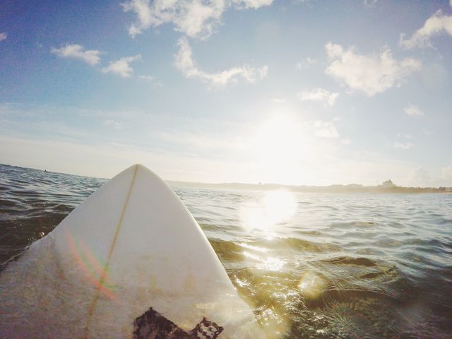 Image captures the calm ocean with a surfboard pointing towards the rising sun on the horizon. Keywords emphasize the serene morning setting ideal for surfing enthusiasts. Great for use in travel blogs, sports equipment promotions, beach resort advertisements, and social media posts promoting outdoor activities and water sports.