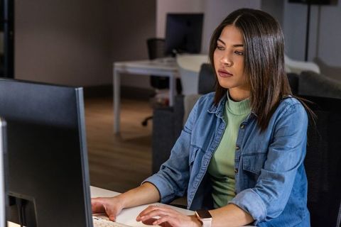 Focused asian woman working on desktop computer at modern office desk with smartwatch