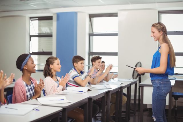 Students are applauding a classmate after a presentation in a classroom. This image can be used to depict educational settings, student interactions, teamwork, and academic achievements. It is ideal for educational websites, school brochures, and articles about student life and learning environments.