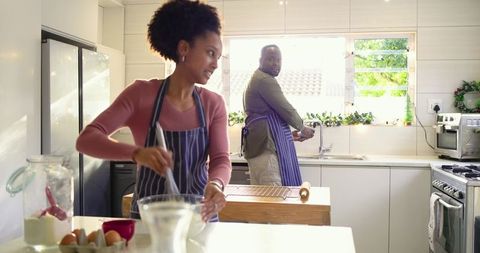 Couple Baking Together in Bright Modern Kitchen Whisking Batter While Partner Washes Hands