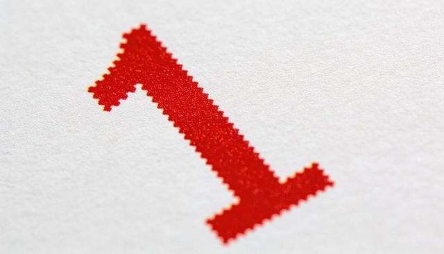 Macro closeup red serrated halftone numeral 1 on textured white paper showing print grain