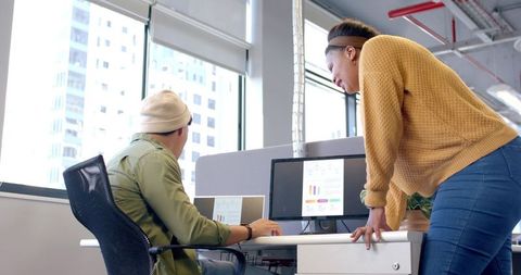 Diverse coworkers collaborating and reviewing analytics on laptop and monitor in office