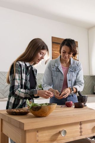 Two women preparing fresh salad at wooden kitchen island, casual home cooking
