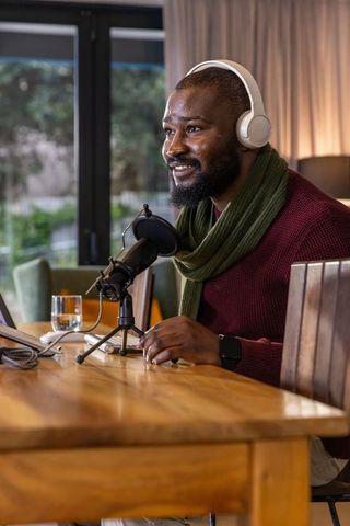 African american man recording cozy home podcast wearing headphones and speaking into mic