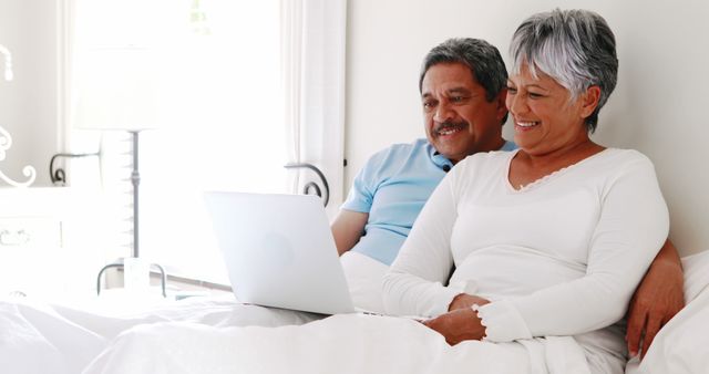 Senior couple relaxing in bed using a laptop, symbolizing technology use among older adults. Perfect for showcasing themes of retirement, leisure, and modern lifestyle among seniors. Useful for articles about senior living, health and wellness, and technology adoption in the elderly community.