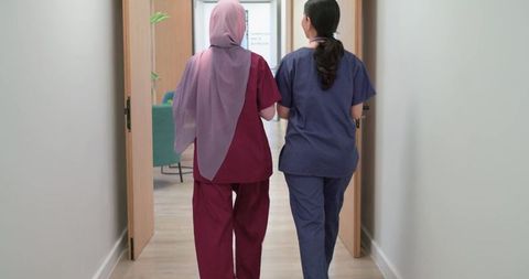 Diverse female medical staff walking down clinic corridor wearing maroon and navy scrubs