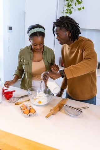 African american couple preparing batter in modern kitchen pouring milk into mixing bowl